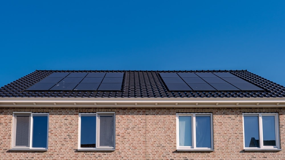 A brick house with four windows and solar panels installed on its dark tiled roof under a clear blue sky—perfectly showcasing Solar Panels St. John the Baptist Parish.