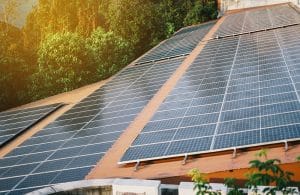 Rows of solar panels are installed on a sloped orange roof surrounded by green foliage in St. John the Baptist Parish, capturing sunlight for renewable energy.
