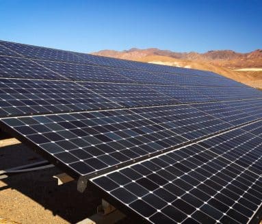 Rows of solar panels installed in a desert environment highlight the growth of solar in California, with mountains and a clear blue sky in the background.